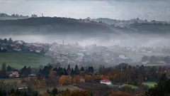 Mlha zahaluje údolí s městem v dálce pod mraky