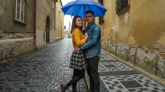 Mladý pár s modrým deštníkem na historické dlažbě města v dešti