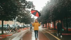 Žena s deštníkem ve žluté bundě kráčí po mokré městské ulici v deštivém počasí.